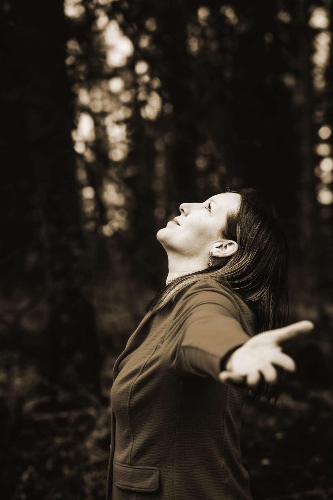Åsa-Malin standing in the forest with arms open and face lifted to the light.