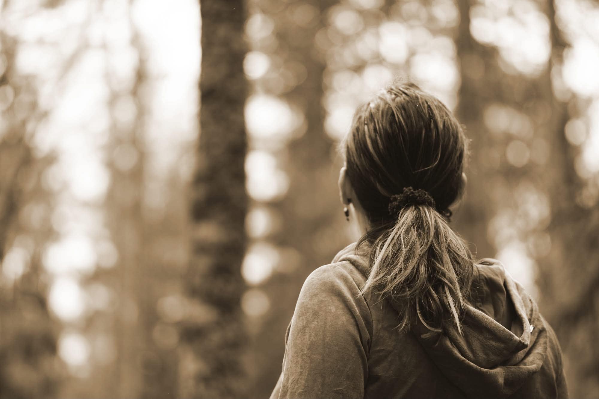 A woman standing quietly in a forest, seen from behind, taking a breath alone.